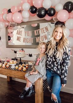 a mother and daughter sitting at a table in front of some cupcakes with balloons