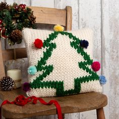 a knitted christmas tree pillow sitting on top of a wooden chair next to a pine cone