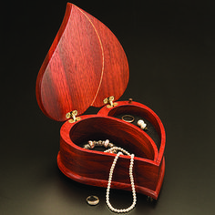 an open wooden box with jewelry inside on a black surface in front of a white bead necklace