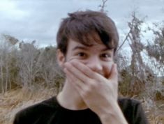 a young man covers his mouth with his hands while standing in the middle of a field