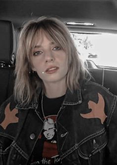 a woman sitting in the back seat of a car wearing a jean jacket and piercings