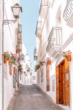 an alley way with white buildings and flowers on the windows