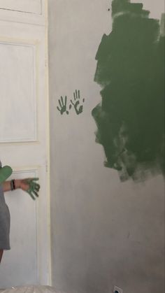 a woman painting a wall with green paint and hands prints on the wall behind her