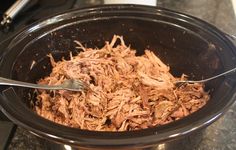 shredded meat in a slow cooker with tongs on the side and fork sticking out of it