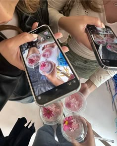 two women are holding up their cell phones with pictures on them and some drinks in front of them