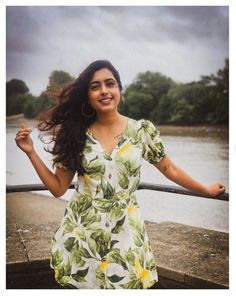 a woman in a dress is standing by the water with her arms out and smiling