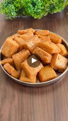 a bowl filled with cubed food sitting on top of a wooden table next to a potted plant