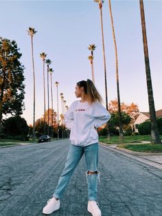 a woman standing in the middle of an empty street with palm trees behind her,