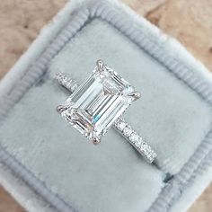 an emerald - cut diamond ring sits in a velvet box on top of a carpeted surface