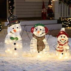 three snowmen with hats and scarfs are standing in the snow, surrounded by christmas lights