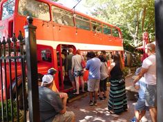 people are standing in front of an orange double - decker bus and looking at it