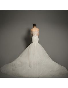 a woman in a white wedding dress standing against a gray wall with her back turned to the camera