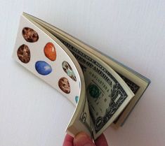 a hand holding an open money bill with magnets on it's side, in front of a white background