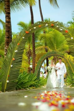 a bride and groom walking down the aisle with palm trees in the background at their wedding