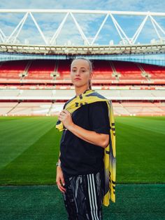 a woman standing in front of an empty soccer stadium with her scarf around her neck