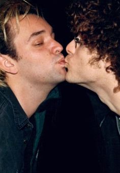 two men are kissing each other while one is wearing glasses and the other has curly hair