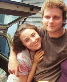 a man and woman sitting next to each other in front of a car