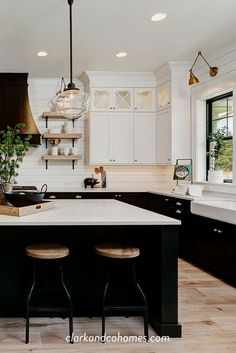 a kitchen with black cabinets and white counter tops, two stools at the island