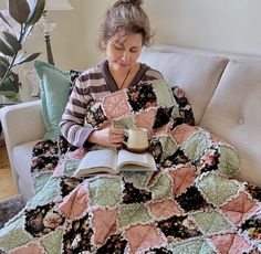 a woman sitting on a couch reading a book and holding a coffee cup in her hand