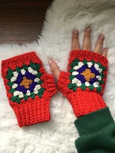 a woman's hand wearing red crocheted mitts on top of a white rug