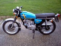 a blue and black motorcycle parked on top of a parking lot next to green grass