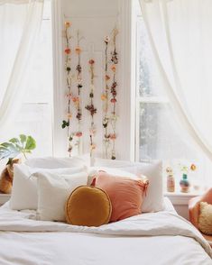 a bed with white sheets and pillows in front of a window filled with hanging flowers