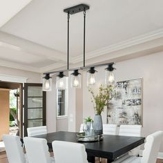 a dining room table with white chairs and lights hanging from the chandelier above it