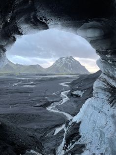 an ice cave with mountains in the background and water running through it, as seen from inside