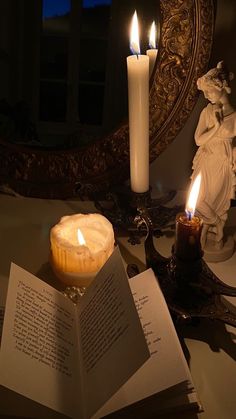 an open book sitting on top of a table next to two lit candles and a mirror