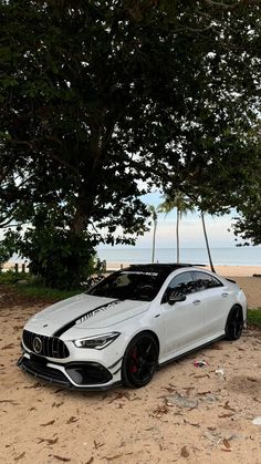 a white car parked on top of a sandy beach next to trees and the ocean