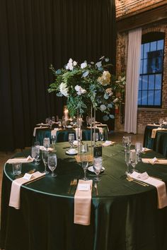 the table is set up with green linens and white flowers in tall vases