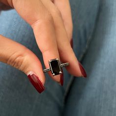 a woman's hand with red nail polish holding a black and white diamond ring