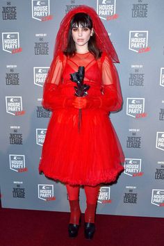 a woman in a red dress and veil poses for the camera on a red carpet