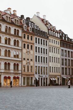 people are walking in front of several buildings on a cobblestone street with an umbrella