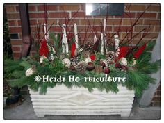 a white planter filled with lots of greenery and christmas decorations in front of a brick wall