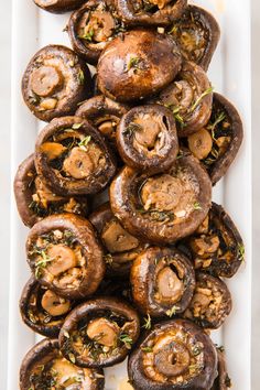 mushrooms piled on top of each other in a white dish with herbs and seasoning