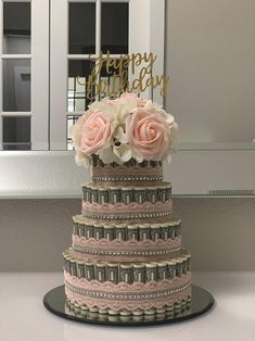 a three tiered cake decorated with pink roses and dollar bills is shown in front of a window