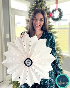 a woman holding a paper snowflake in front of a christmas tree