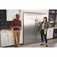 a man and woman standing in front of a stainless steel refrigerator