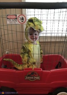 a toddler in a dinosaur costume sitting in a red wagon with the words, dinosaurs on it