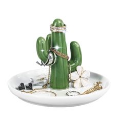 a green cactus shaped jewelry holder on a white plate with other accessories around it and the top part of its body visible