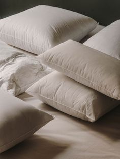 four pillows stacked on top of each other in front of a bed with white sheets