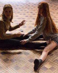 two women sitting on the floor talking to each other with their hands out in front of them