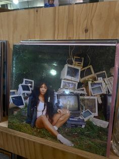 a woman sitting on top of a wooden shelf next to a pile of old televisions