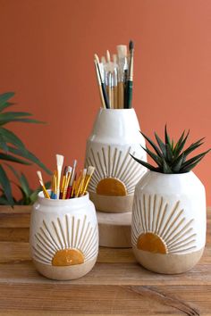 three white vases with plants and pencils in them on top of a wooden table