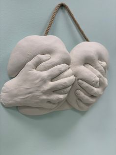 two white hands holding each other on a blue wall hanging from a rope with twine