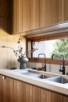 a vase with flowers in it sitting on a kitchen counter next to a sink and window