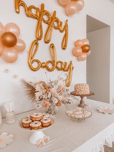 a table topped with donuts and balloons next to a wall that says happy baby