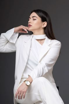 a woman sitting on top of a black chair wearing a white suit and matching watch