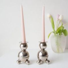 two silver candlesticks sitting next to each other on a white surface with a flower in the background